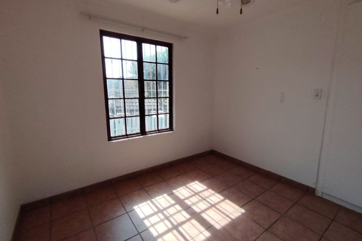 A vacant bedroom featuring tiled flooring, a ceiling fan, and a window fitted with security bars.