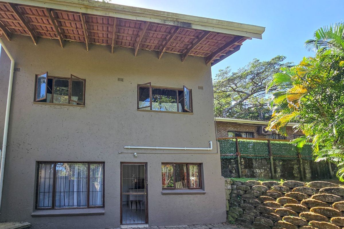 Rear elevation of a two-story house featuring exposed rafter eaves, terracotta roof tiles, and a paved patio area with a stone retaining wall.