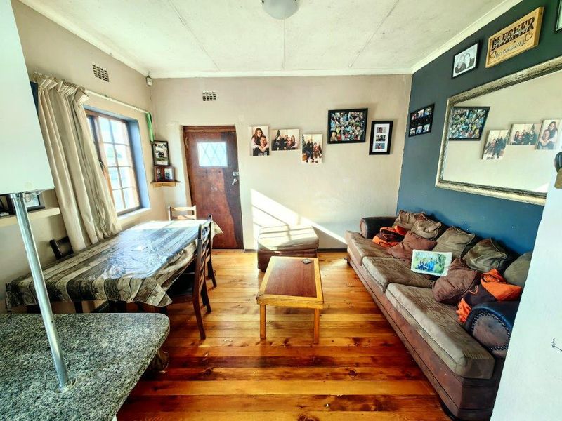 Open plan living and dining area featuring timber flooring, granite kitchen counter, and direct access to the exterior via a timber door.