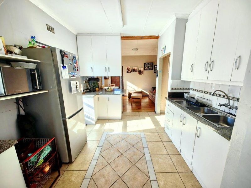 A functional kitchen featuring white built-in cabinetry, double bowl sink, and tiled flooring, with an open layout leading into the adjacent living area.