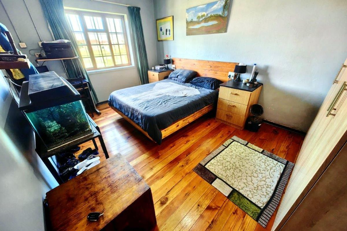 A bedroom featuring polished timber flooring, a built-in wardrobe, and a multi-pane window providing natural light.
