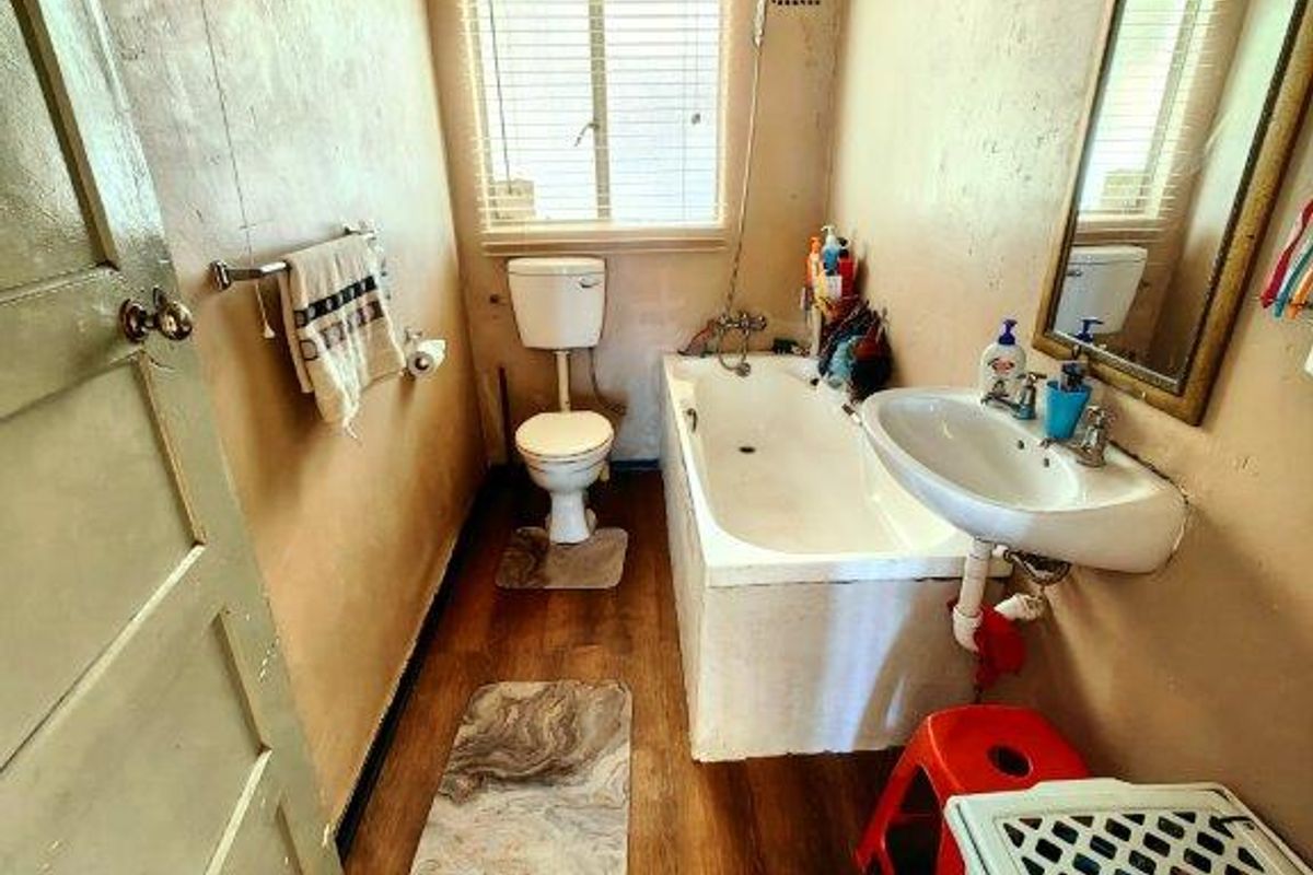 A compact bathroom featuring a bathtub, wall-mounted basin, and toilet, requiring cosmetic updates to the walls and ceiling to improve its overall condition.