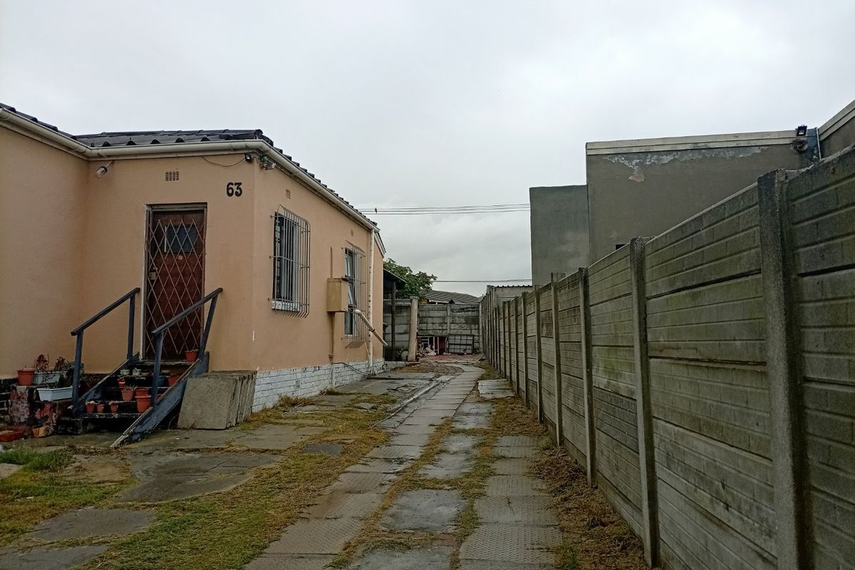 Side view of the property showing a paved driveway, precast concrete boundary wall, and exterior access to the building with security features.