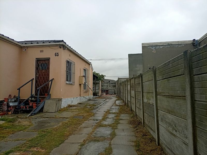 Side view of the property showing a paved driveway, precast concrete boundary wall, and exterior access to the building with security features.