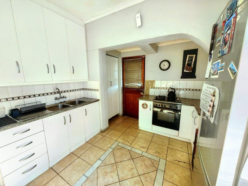 Functional kitchen featuring white cabinetry, tiled flooring, built-in oven and gas hob, with a practical layout and direct access to an exterior door.