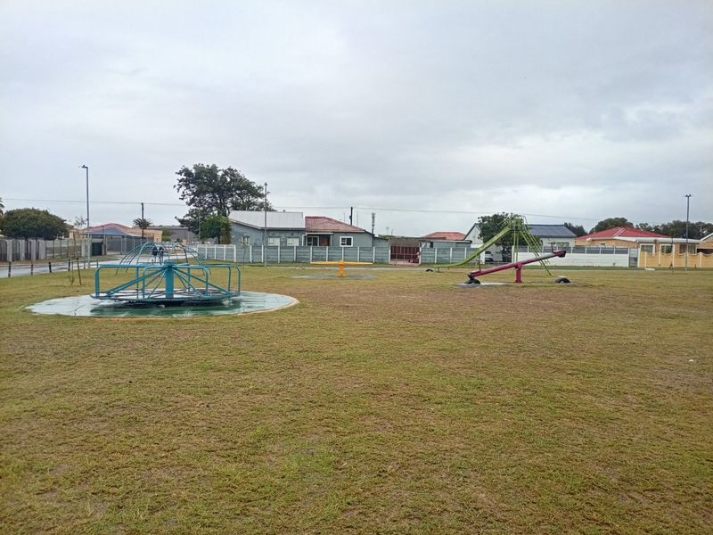 A communal outdoor playground area featuring fixed play equipment, set within a residential neighborhood with perimeter walling.