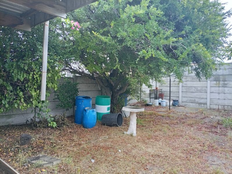 A rear garden area featuring a precast concrete boundary wall, mature tree, and rotary clothesline, currently requiring landscaping and maintenance.