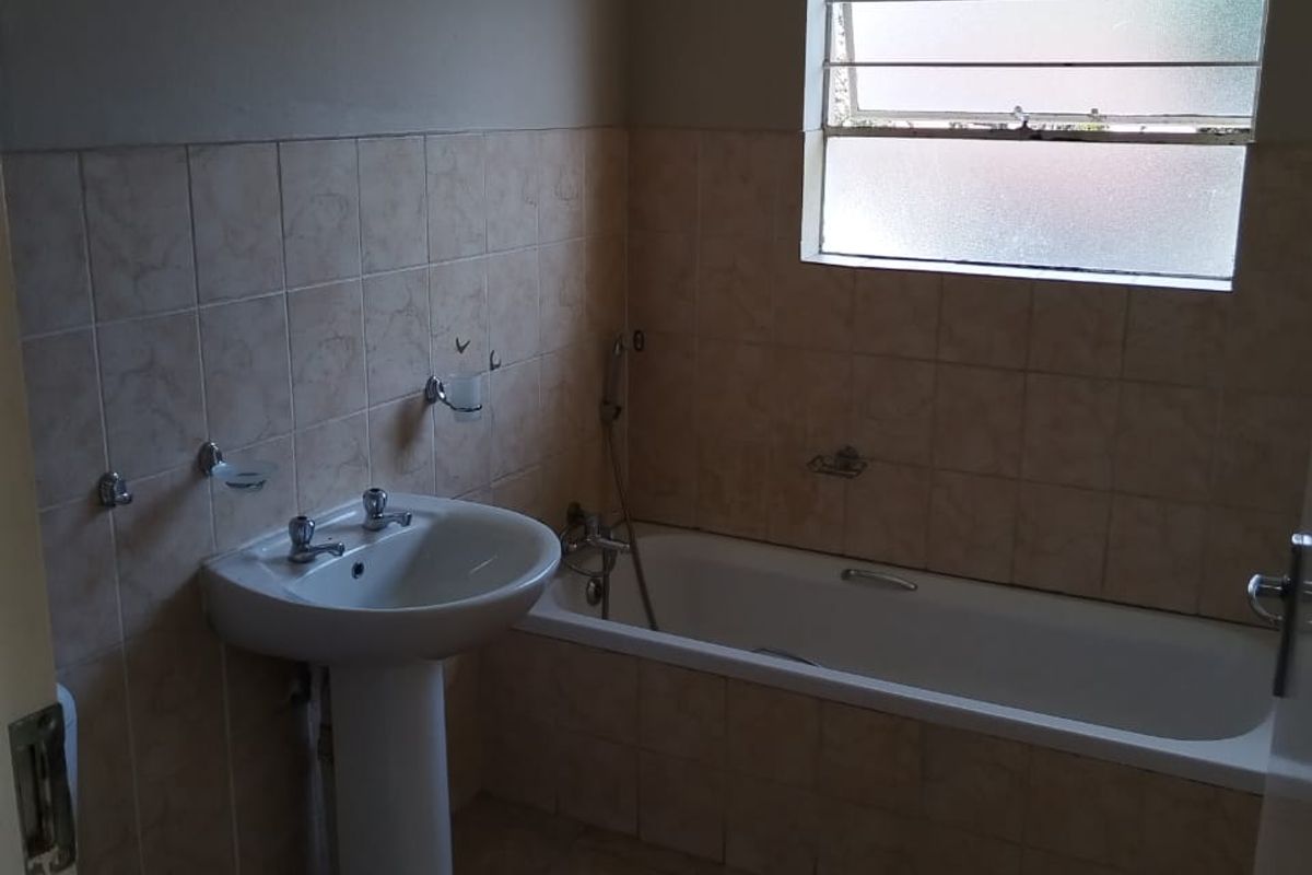 A functional bathroom featuring a pedestal basin, a standard bathtub with shower mixer, and neutral wall and floor tiling.