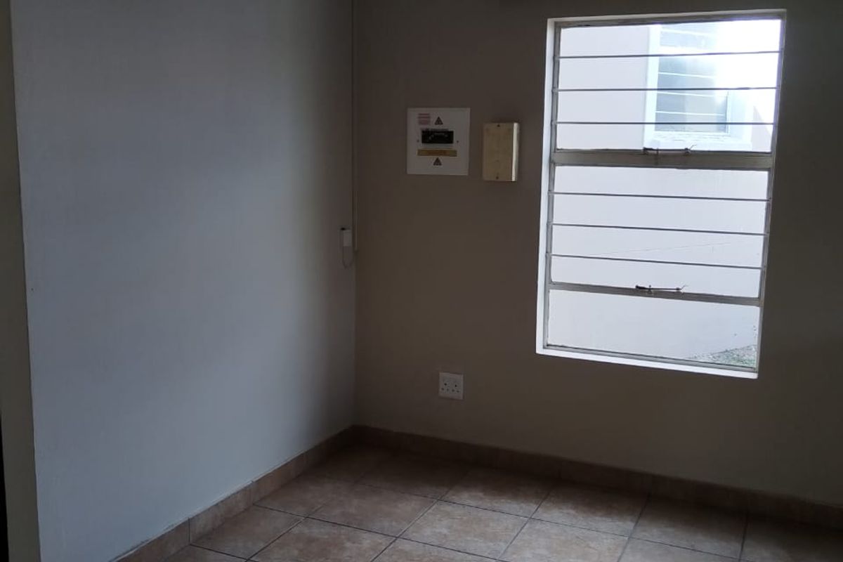 An empty room featuring neutral wall paint, tiled flooring, a window with security bars, and a wall-mounted electrical distribution board.