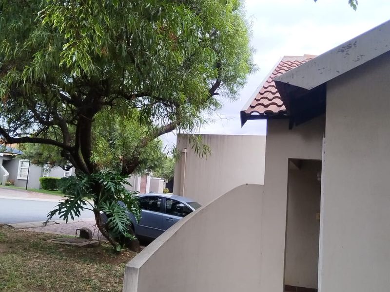 Exterior view of the property entrance featuring a curved masonry wall, tiled roof section, and paved walkway surrounded by established trees.