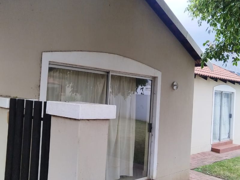 A view of the rear exterior of the house featuring paved patio areas, sliding glass doors, and a small garden space.