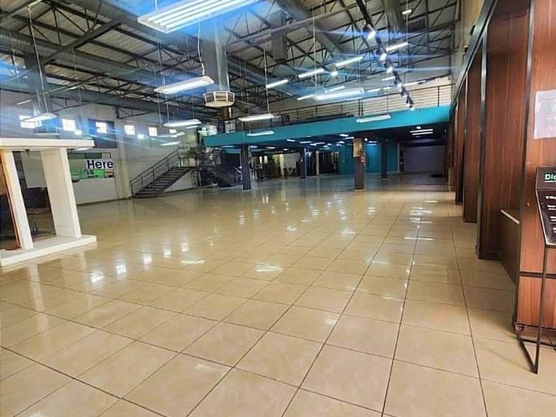 Spacious open-plan commercial interior featuring high ceilings with exposed steel trusses, tiled flooring, and a mezzanine level with a metal staircase.