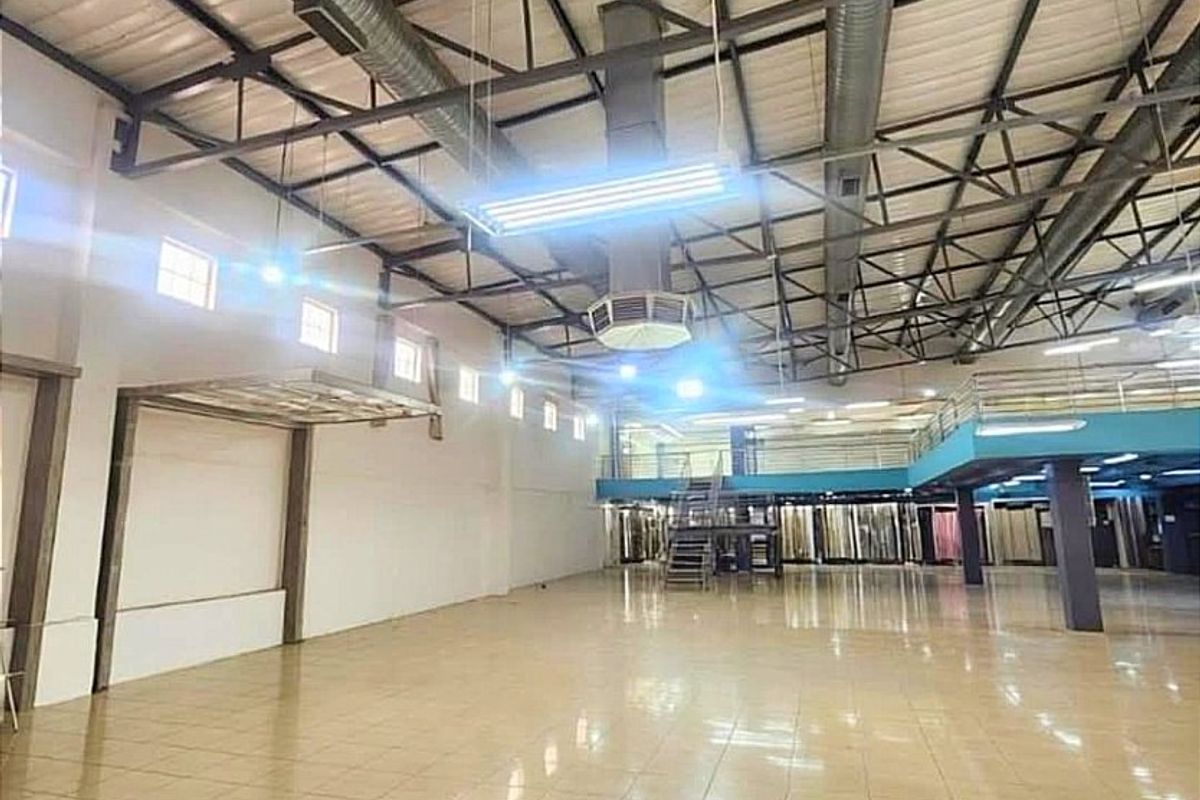 Spacious commercial warehouse or showroom featuring high ceilings with exposed steel trusses, tiled flooring, a mezzanine level, and integrated HVAC ducting.