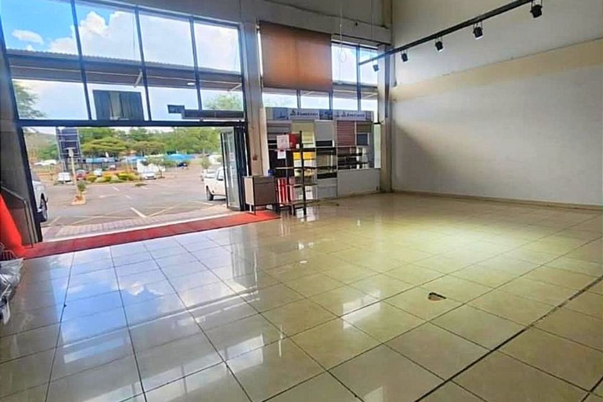 Spacious open-plan commercial unit featuring high ceilings, large glass storefront windows, tiled flooring, and industrial lighting, suitable for retail or showroom use.