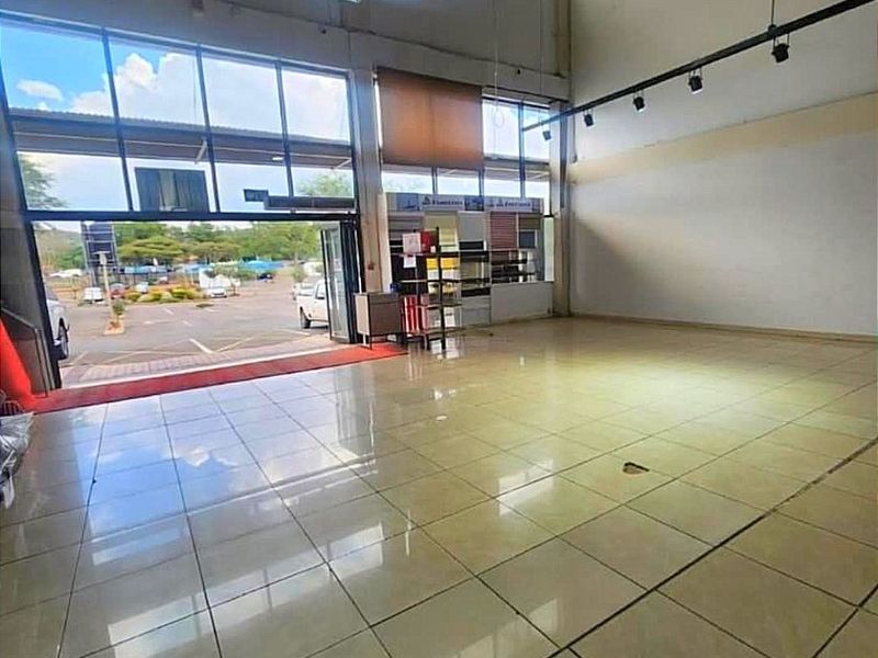 Spacious open-plan commercial unit featuring high ceilings, large glass storefront windows, tiled flooring, and industrial lighting, suitable for retail or showroom use.