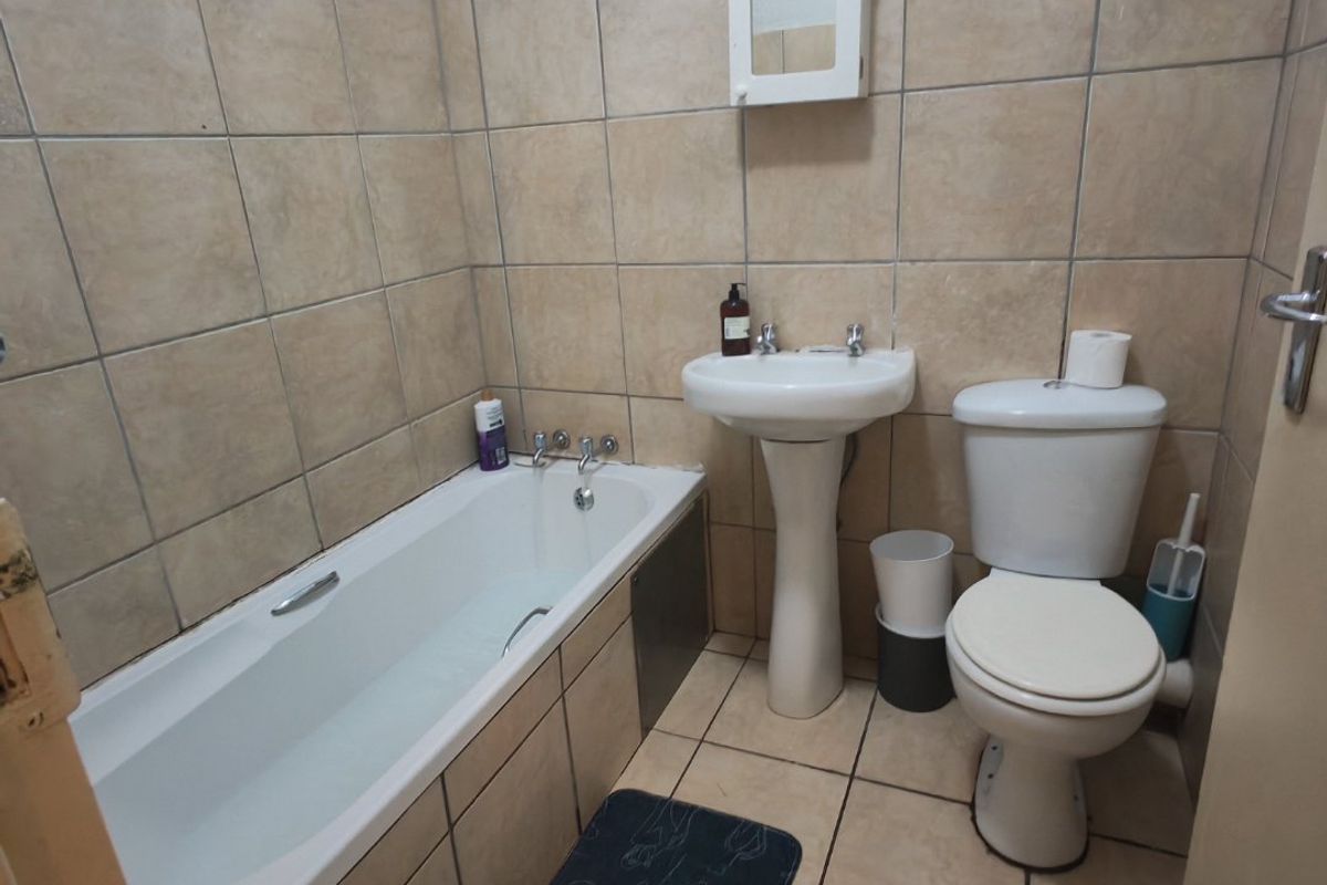 A functional bathroom featuring a standard bathtub, pedestal basin, and toilet with neutral wall and floor tiling.