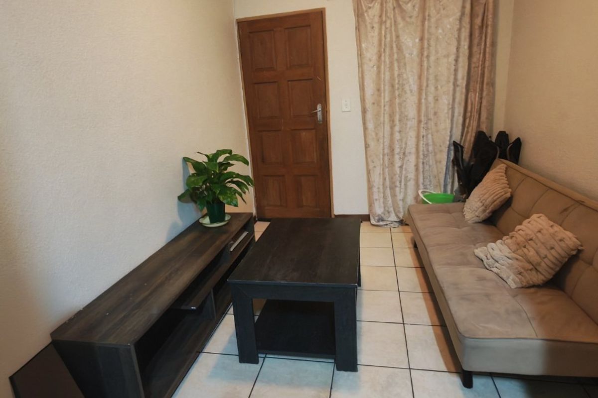 A functional living room featuring tiled flooring, a solid timber door, and a curtained window area, providing a neutral base for interior design.