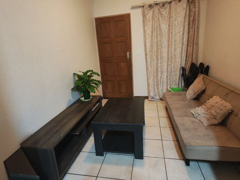 A functional living room featuring tiled flooring, a solid timber door, and a curtained window area, providing a neutral base for interior design.