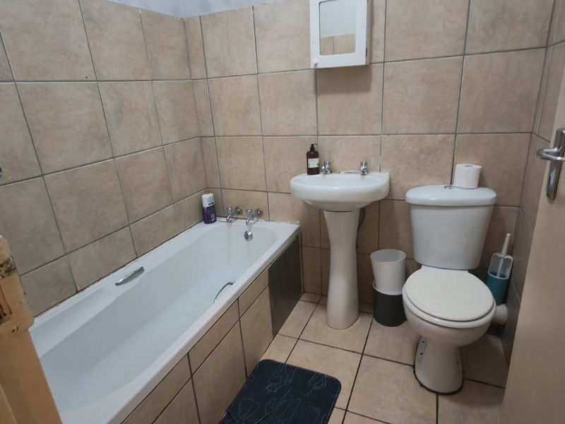 A functional bathroom featuring a pedestal basin, toilet, and bathtub with neutral wall and floor tiling throughout.