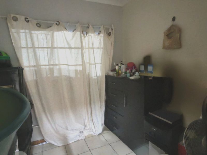 A bedroom featuring tiled flooring and a window fitted with security bars, offering a functional space ready for personalization.
