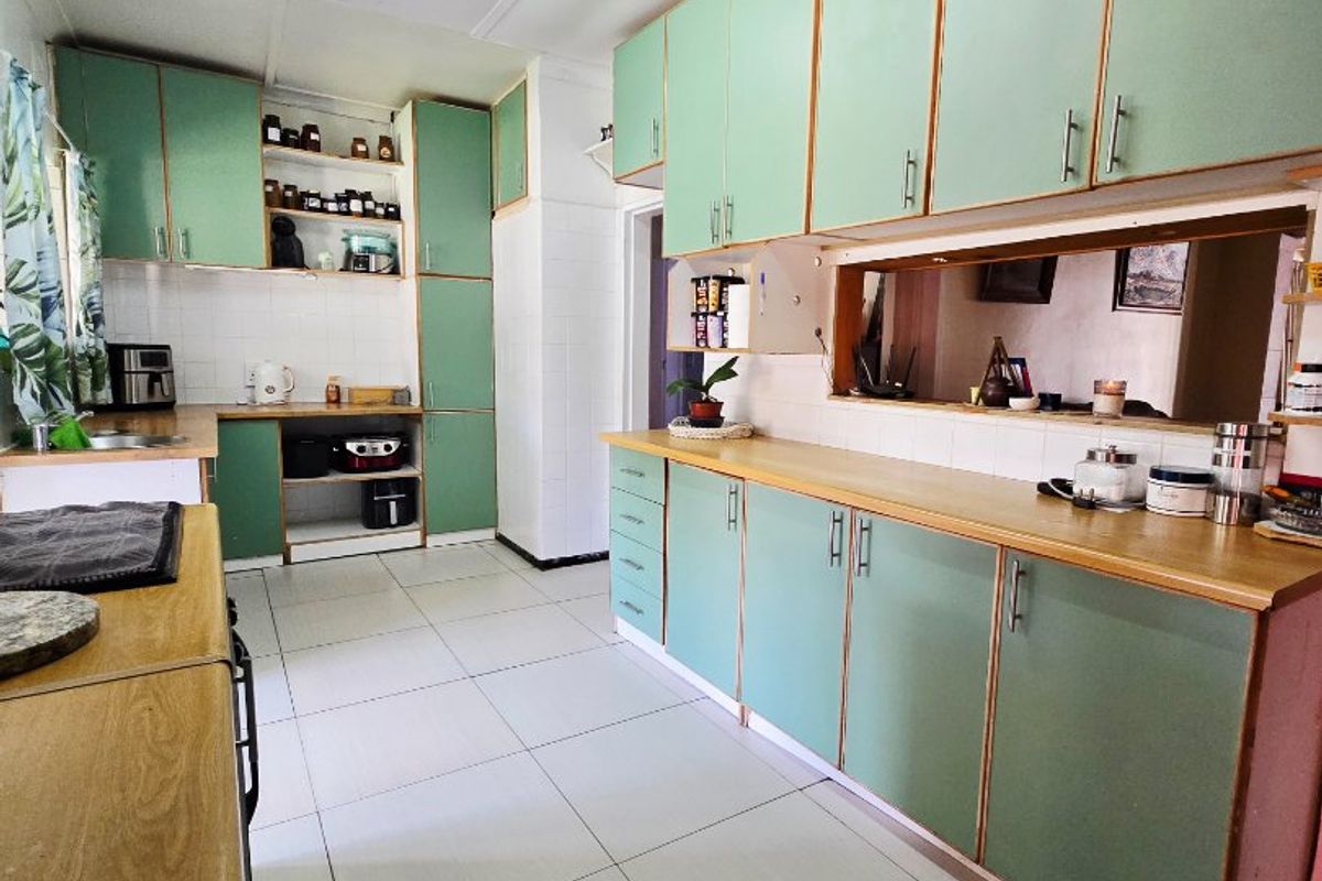 A functional kitchen featuring extensive built-in cabinetry, laminate countertops, tiled flooring, and a convenient serving hatch connecting to the adjacent living space.