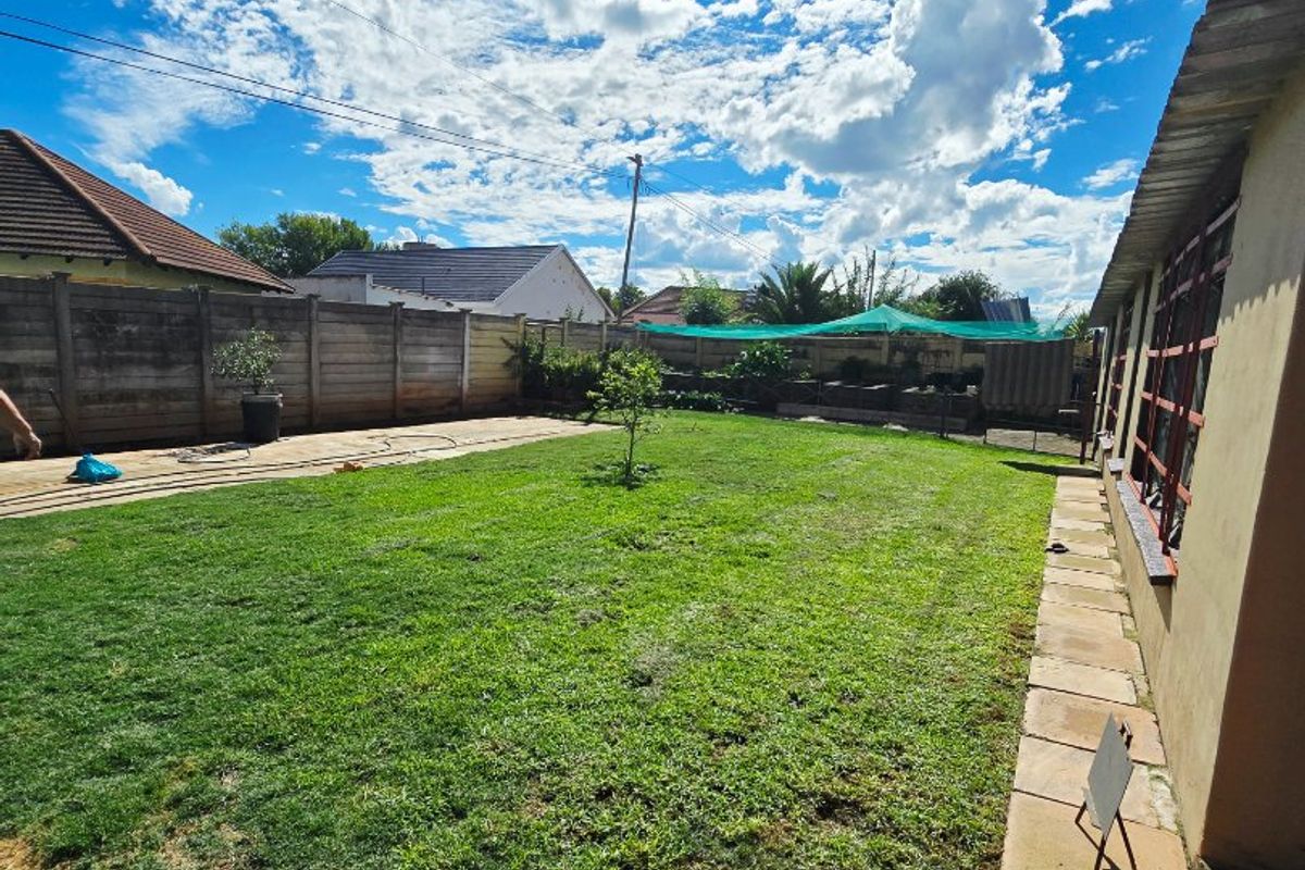 A spacious rear garden featuring a lawn, paved walkway, and secure boundary walling, offering potential for outdoor landscaping and entertainment area development.