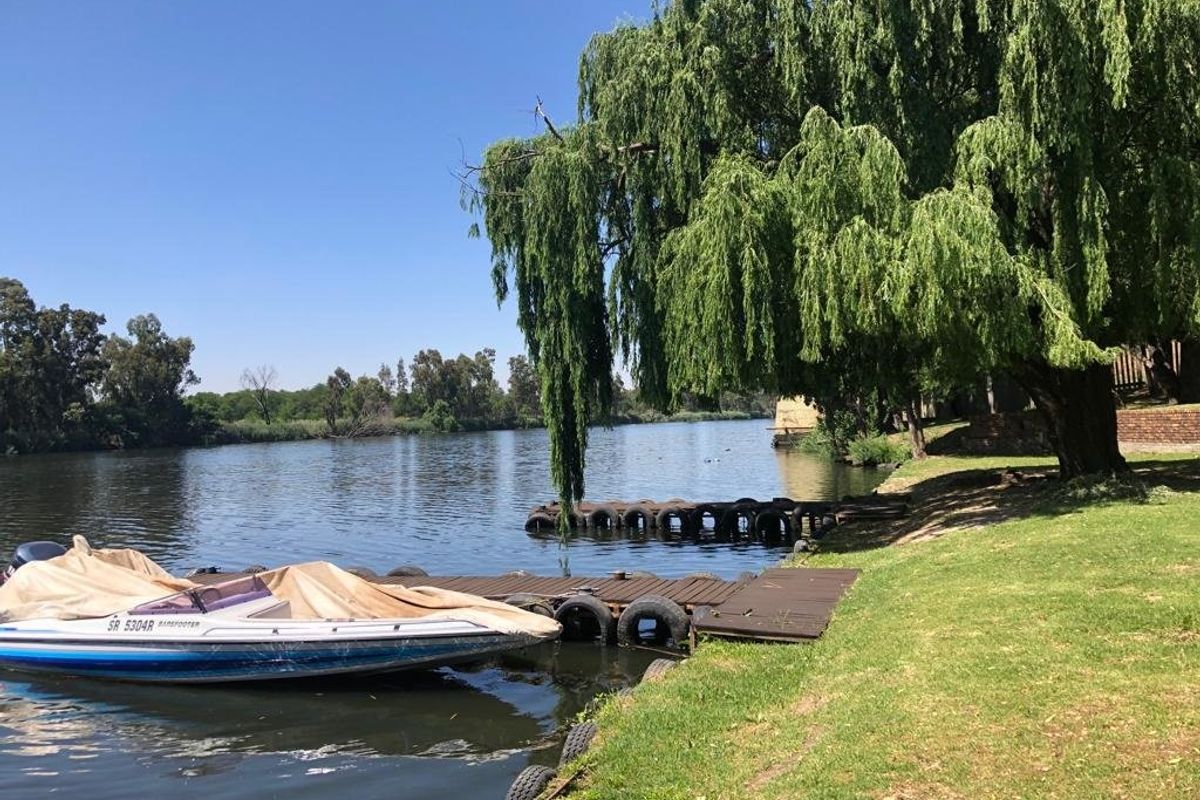 Scenic riverfront view featuring a private jetty, lush green lawn, and a large mature willow tree along the water's edge.