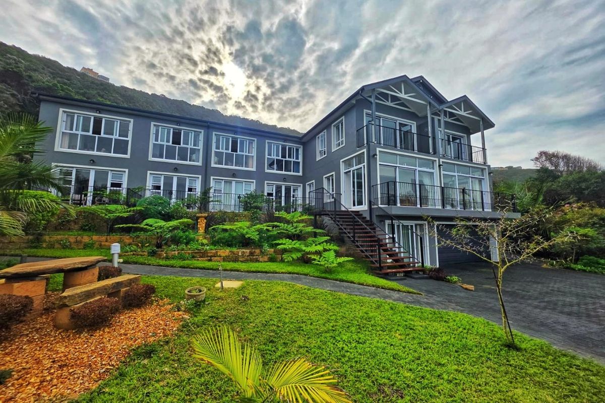 A multi-level residential property featuring a modern grey facade, multiple balconies, and a well-maintained landscaped garden with paved pathways.