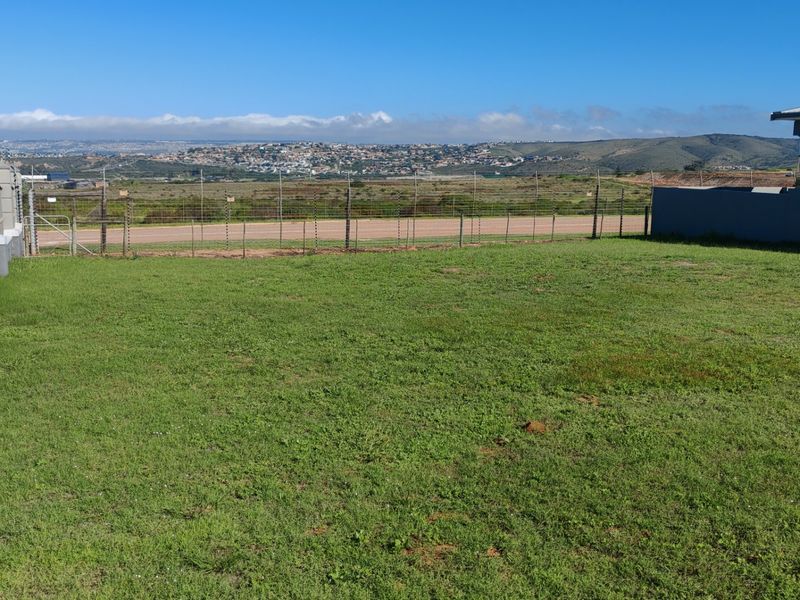 A well-maintained residential plot featuring a grass lawn, perimeter fencing with electric security, and scenic views of the surrounding landscape.