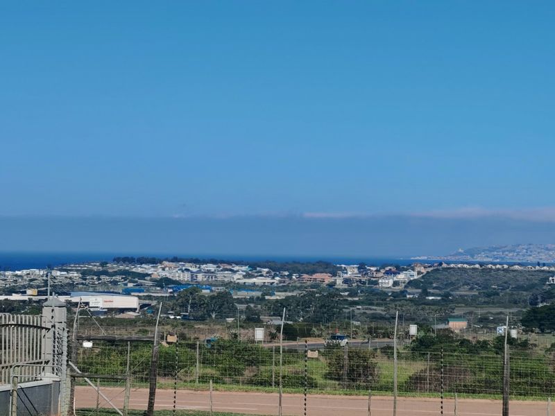 A wide-angle view overlooking the surrounding landscape, residential area, and distant coastline, captured from the property boundary.