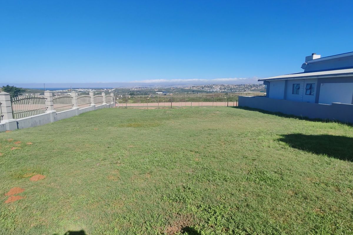 A spacious rear yard featuring a well-maintained lawn, perimeter fencing, and a masonry boundary wall with clear views of the surrounding landscape.