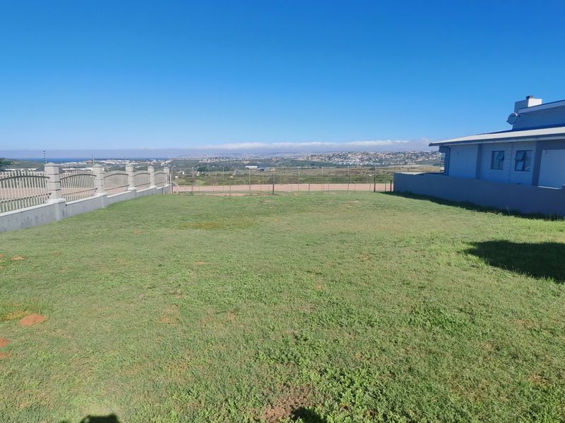 A spacious rear yard featuring a well-maintained lawn, perimeter fencing, and a masonry boundary wall with clear views of the surrounding landscape.