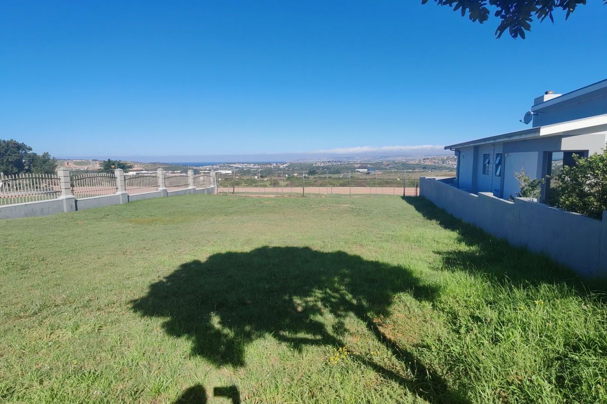 A spacious rear garden area featuring a well-maintained lawn, perimeter walling, and metal fencing, offering an open outlook over the surrounding landscape.
