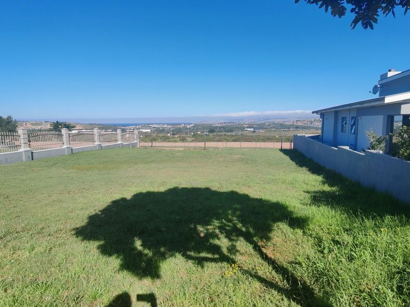 A spacious rear garden area featuring a well-maintained lawn, perimeter walling, and metal fencing, offering an open outlook over the surrounding landscape.