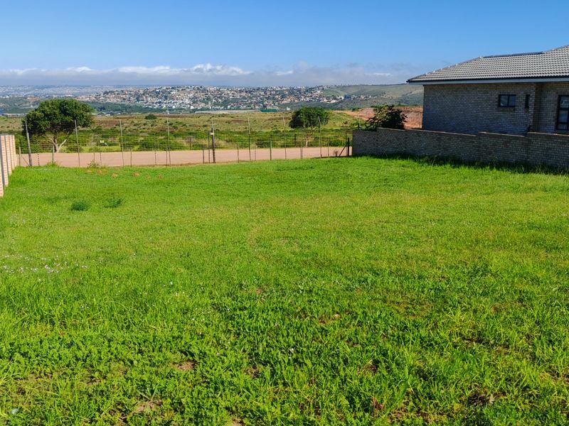 A vacant residential plot featuring a grassy lawn, brick boundary walls, and expansive views of the surrounding landscape and neighborhood.