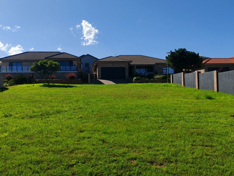 A vacant residential plot featuring a well-maintained grass lawn, enclosed by boundary walls, situated in a developed neighborhood.