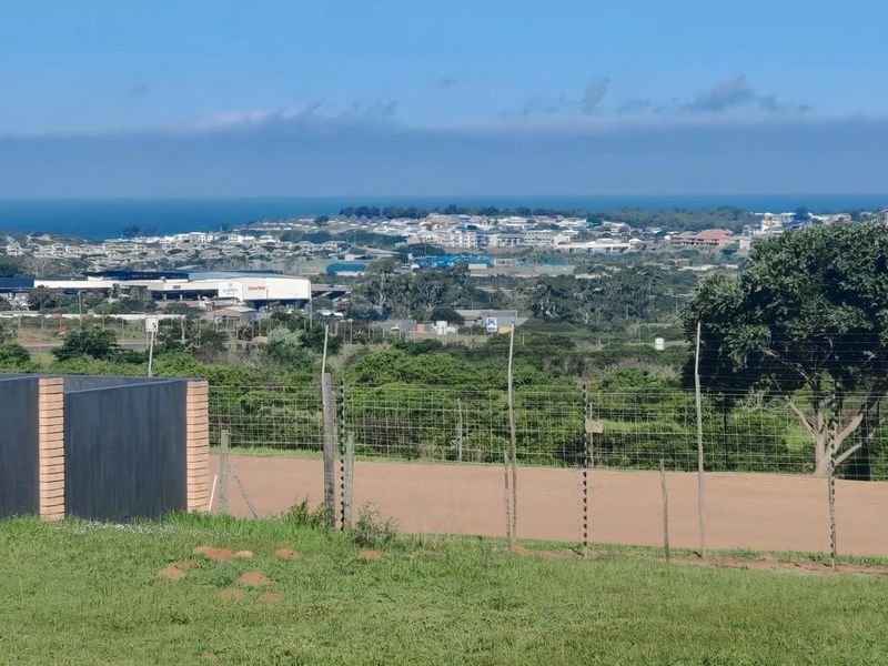 Elevated view overlooking the surrounding landscape, coastal area, and residential development, featuring a boundary wall and electric fencing on the property perimeter.
