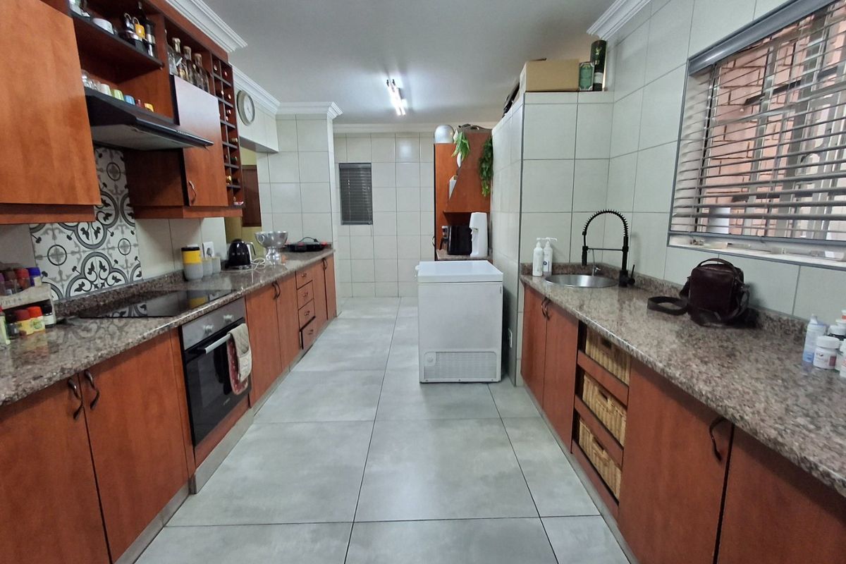 A functional galley-style kitchen featuring wood-finish cabinetry, granite countertops, tiled flooring, and a built-in oven with an extractor fan.