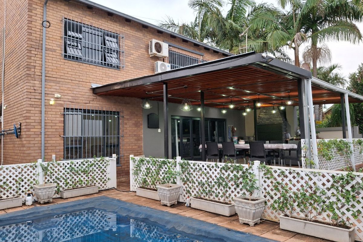 Rear view of a brick house featuring a covered timber patio, swimming pool with cover, and decorative lattice fencing.