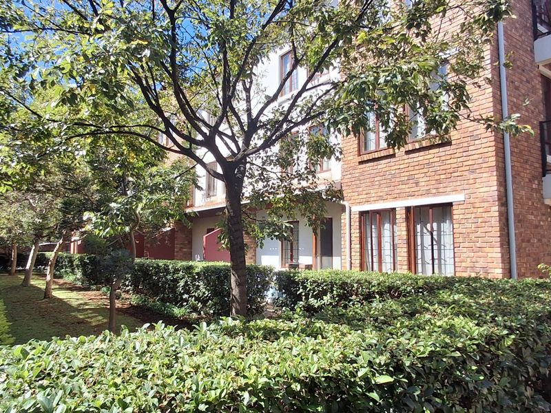 Exterior view of a multi-story apartment complex featuring face brick facades, private balconies, and well-maintained landscaped garden areas.