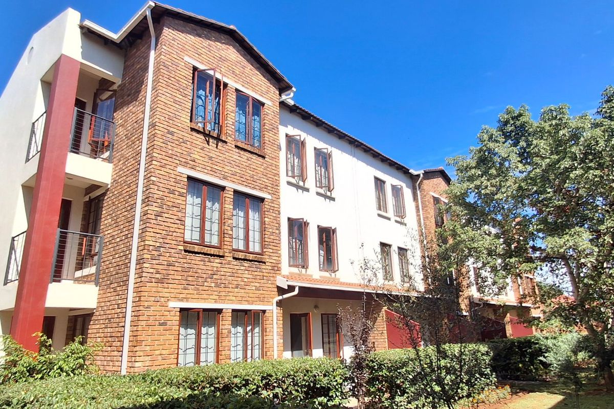 A multi-story apartment building featuring a face brick facade, casement windows, and private balconies with metal railings, set within a landscaped residential complex.