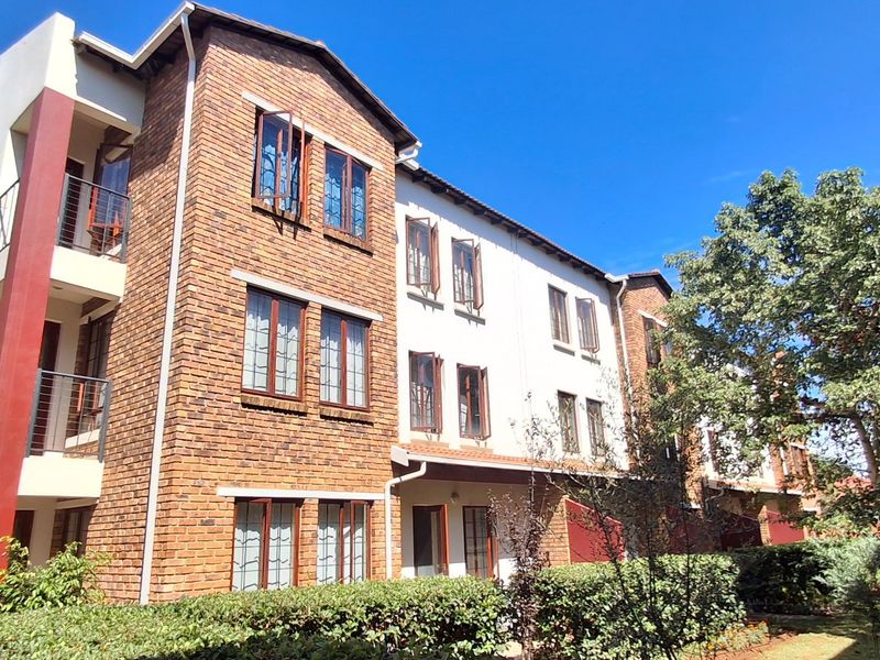 A multi-story apartment building featuring a face brick facade, casement windows, and private balconies with metal railings, set within a landscaped residential complex.