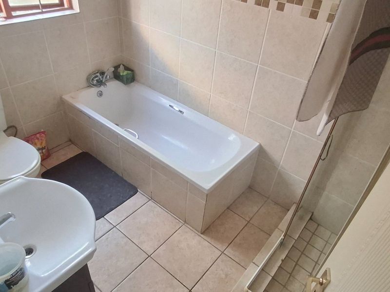 A functional bathroom featuring a bathtub, separate shower enclosure, pedestal basin, and neutral ceramic tiling throughout.