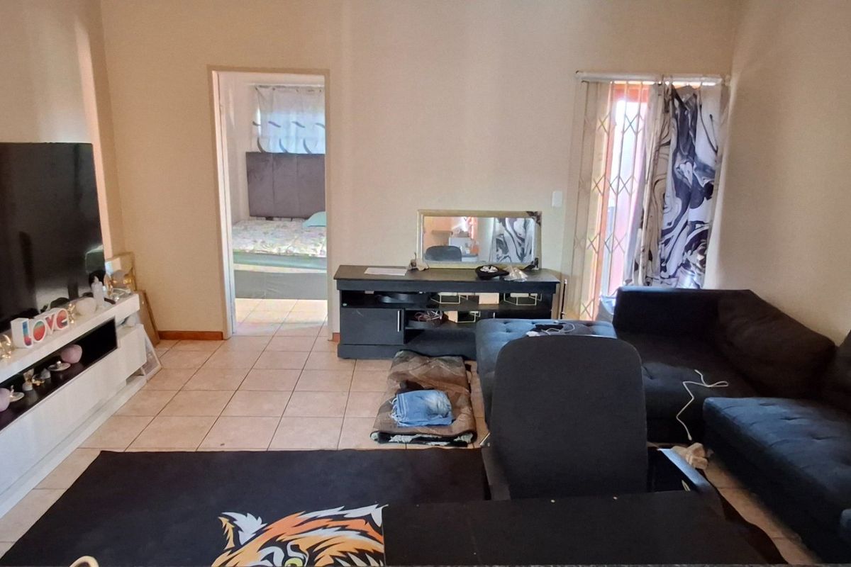 A living room area featuring tiled flooring and access to an adjacent bedroom, with a security gate installed on the exterior door.
