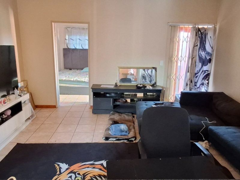 A living room area featuring tiled flooring and access to an adjacent bedroom, with a security gate installed on the exterior door.