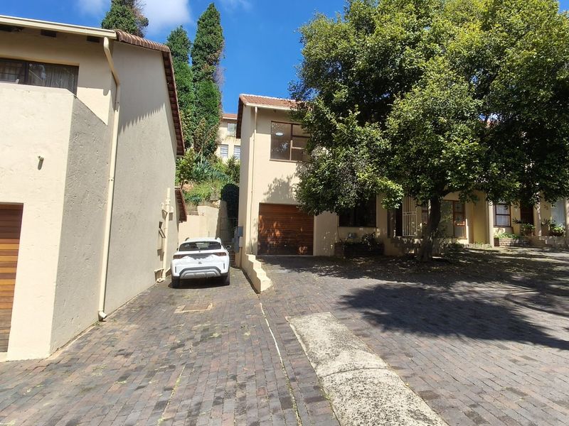 Front exterior view of a townhouse complex featuring paved driveways, garage access, and established trees.