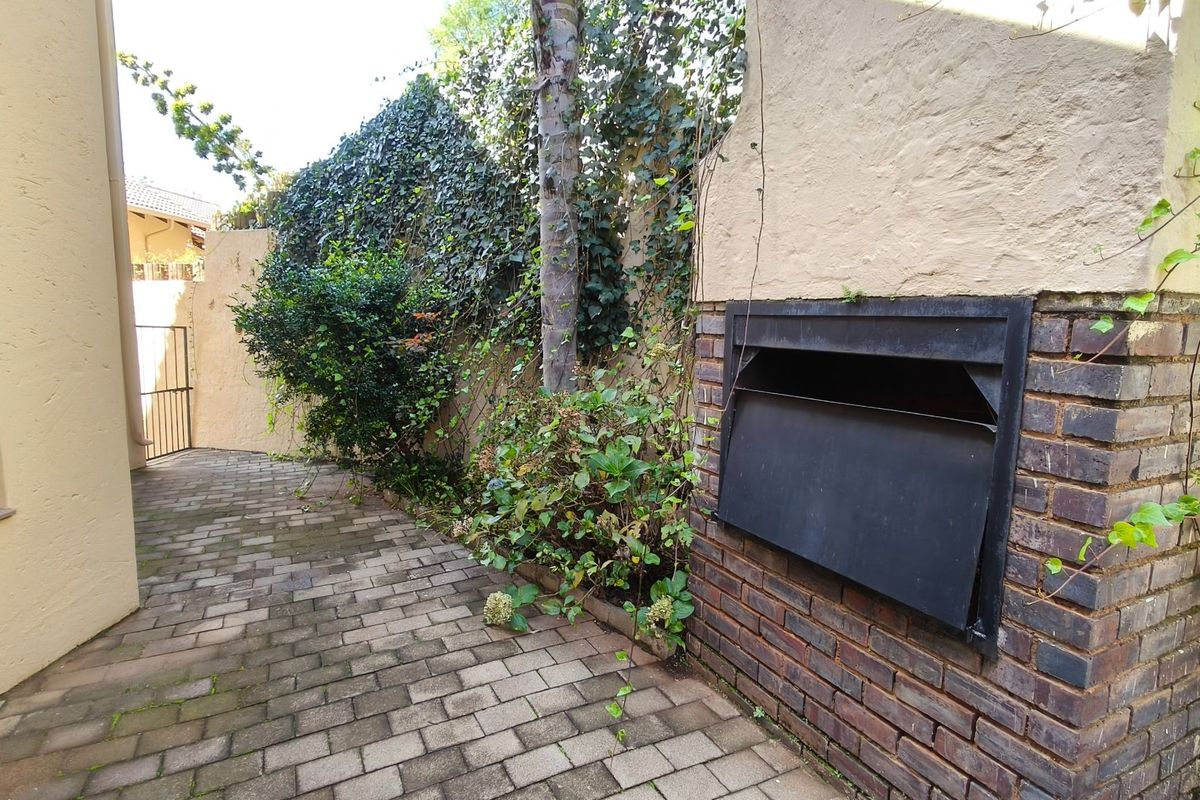 A private rear courtyard featuring brick paving and a built-in braai, surrounded by established boundary walls and climbing greenery.