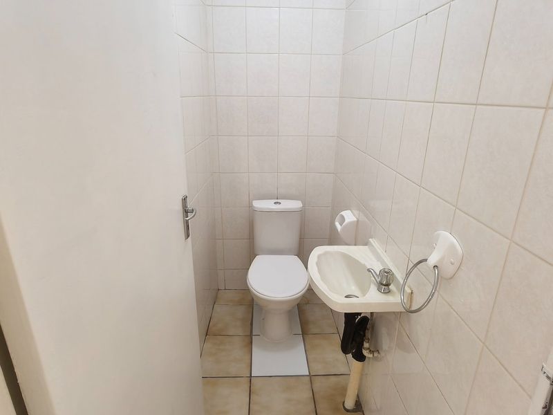 A compact guest bathroom featuring a toilet and a small wall-mounted basin with fully tiled walls and flooring.