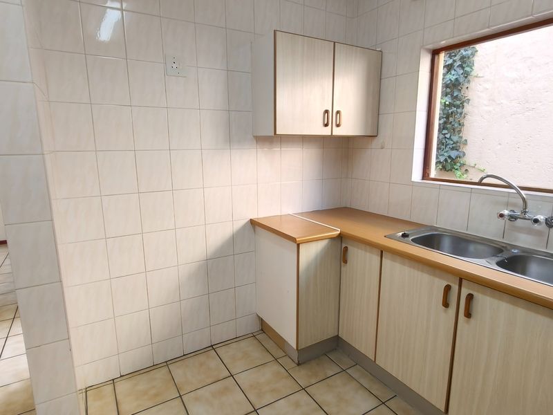 A functional kitchen area featuring tiled walls, laminate cabinetry, and a double bowl stainless steel sink with a view of the exterior.