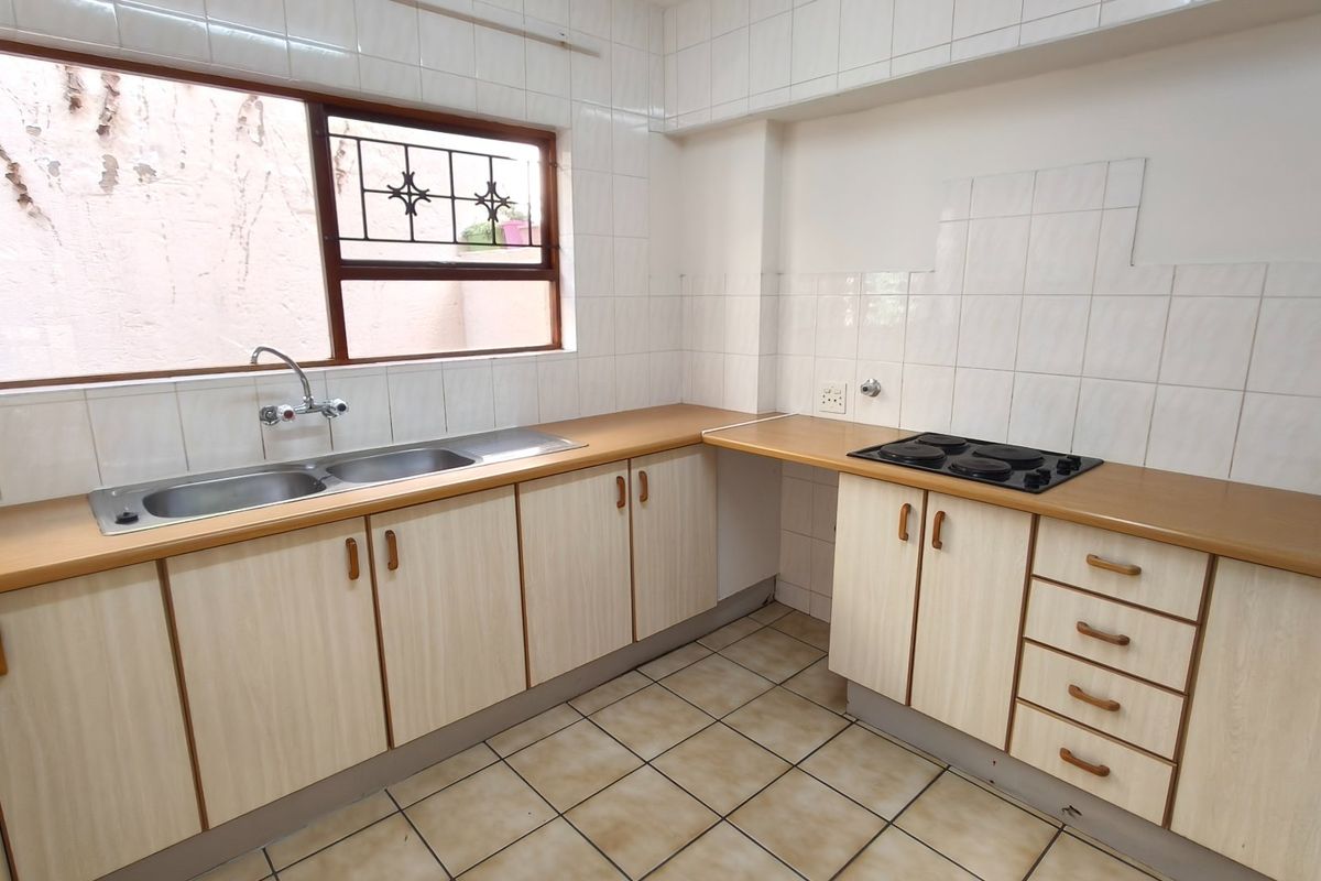 A functional kitchen featuring laminate countertops, built-in cabinetry, a double basin sink, and an electric hob with tiled splashbacks.